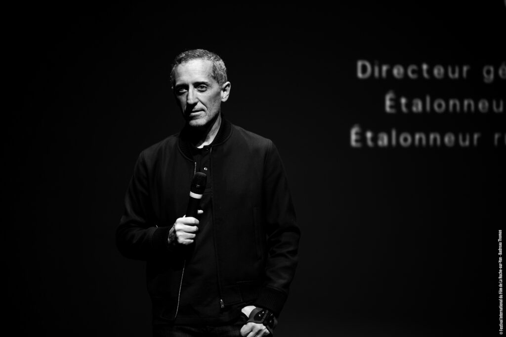photo de Gad Elmaleh noir et blanche sur fond de scène noir