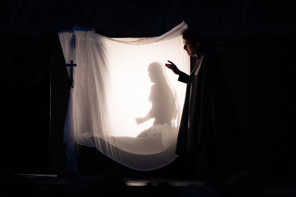 photo en claire obscure, on apperçois une personne devant un rideau blanc derrière lequel la lumière passe et laisse voir l'ombre d'une femme assise