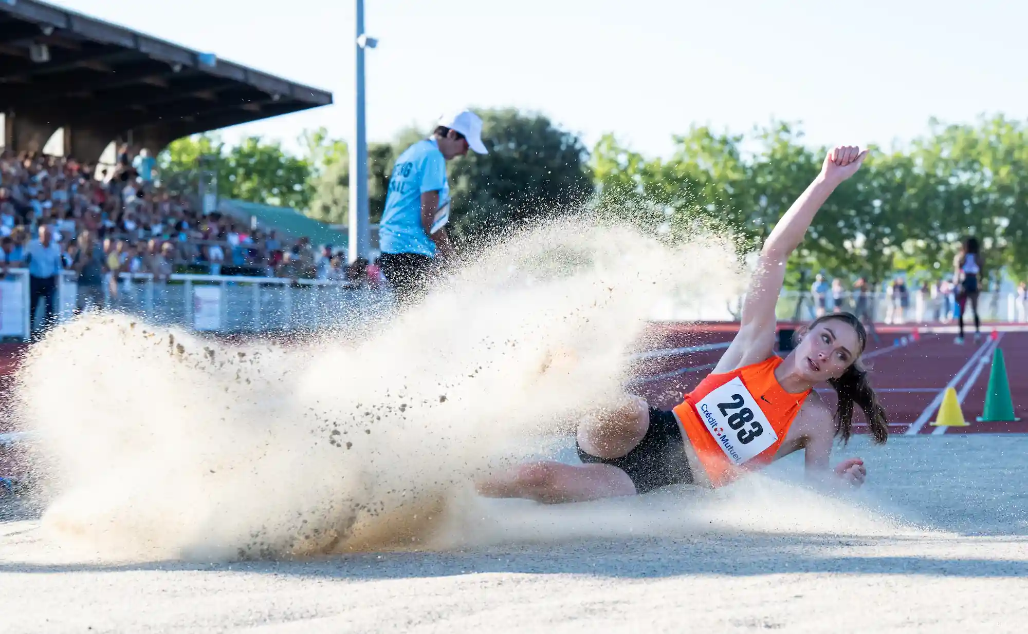 une athlète de saut en longeur attérie dans le sable et le fais jaillir sur fond de stage d'athlétisme
