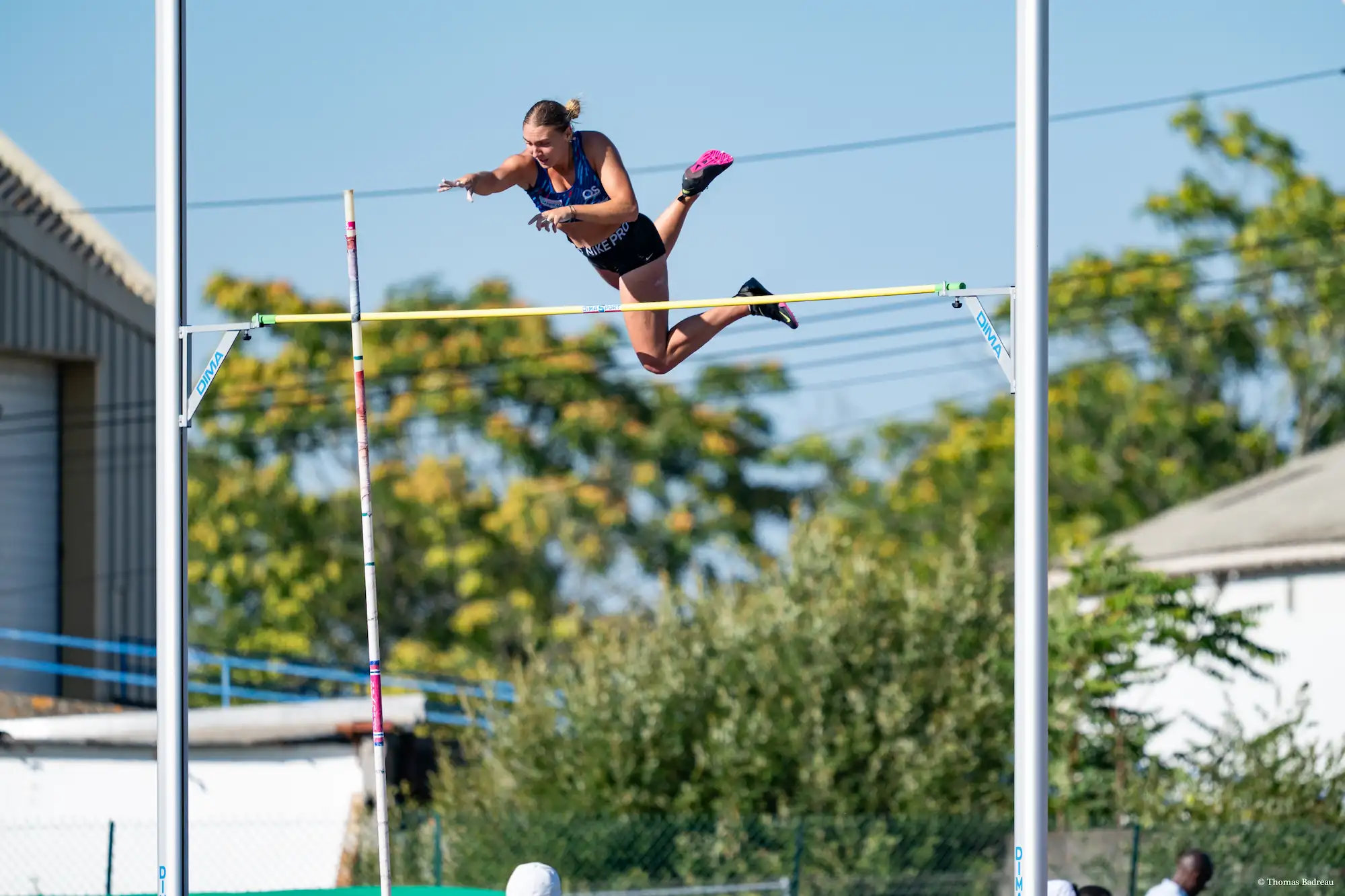 athlète perchiste en plein vol lâchant sa perche au dessus de la barre sur fond d'arbre